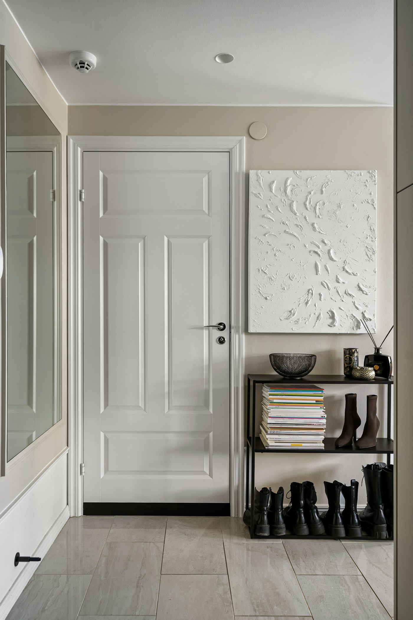 Slim black shelving beside a white door, with a bowl on top and boots stored on the lower shelves.
