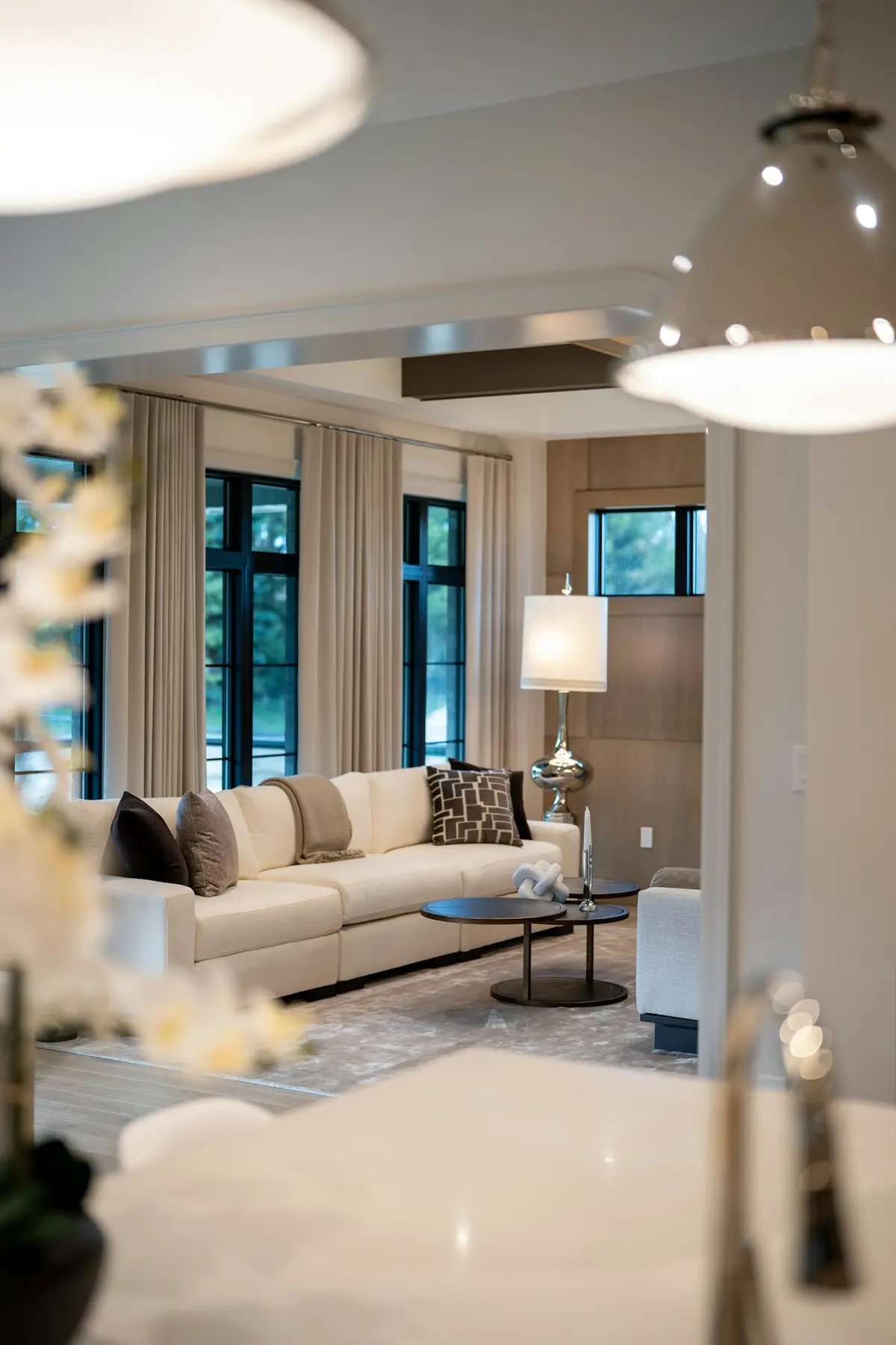 A neutral living room with a sectional sofa, an oval coffee table, a floor lamp and full-height curtains