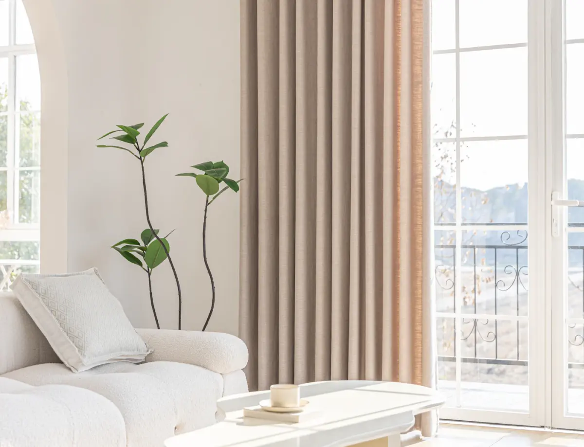 Linen curtains, a boucle sofa and a slender plant beside tall glass doors