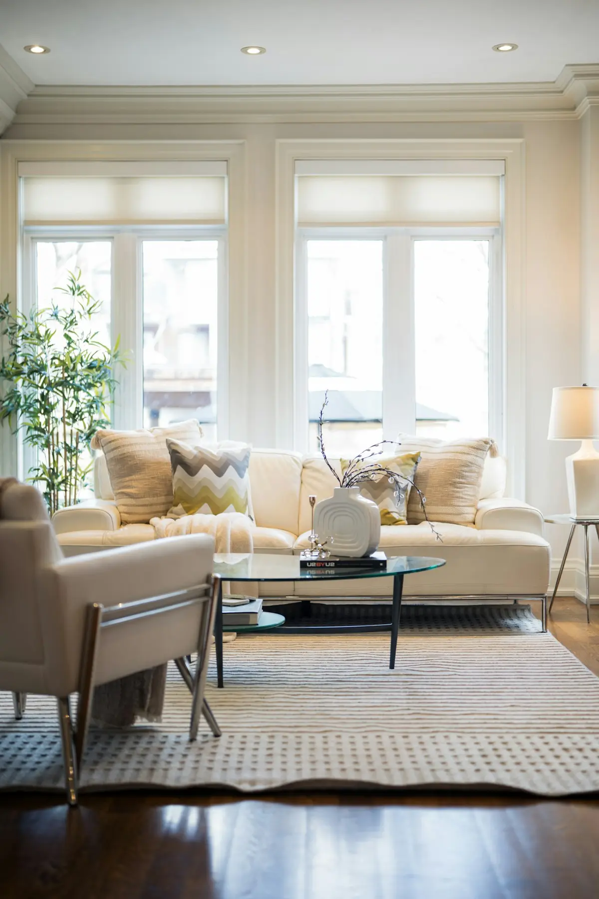 A light-filled seating corner with a cream sofa, armchair, patterned cushions and a glass coffee table