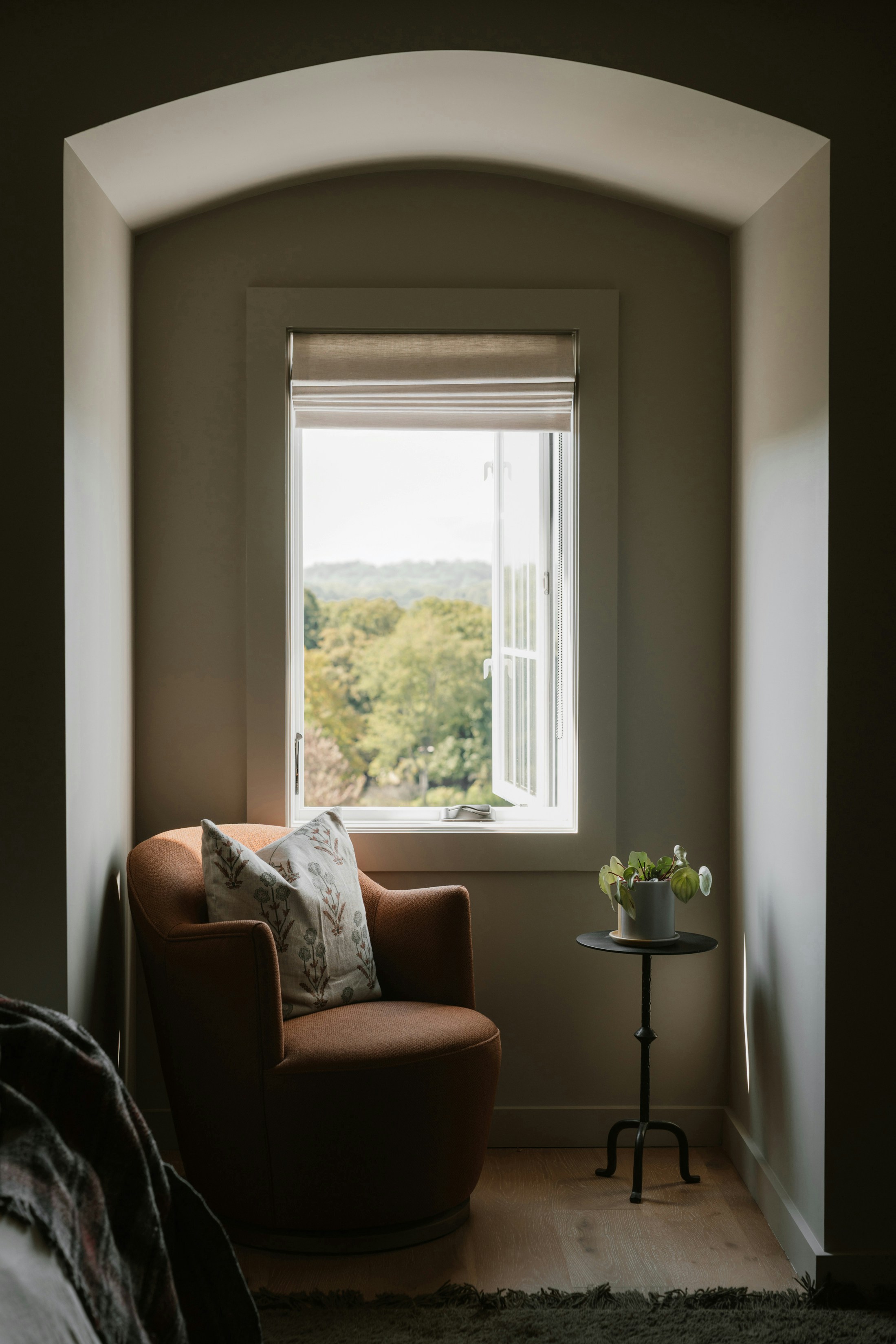 Cozy armchair beside a window overlooking a garden, creating a peaceful reading corner.